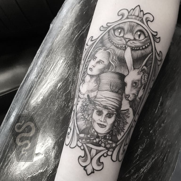Tattoo of 'Alice in Wonderland' characters on a forearm featuring Cheshire Cat, Alice, and Mad Hatter